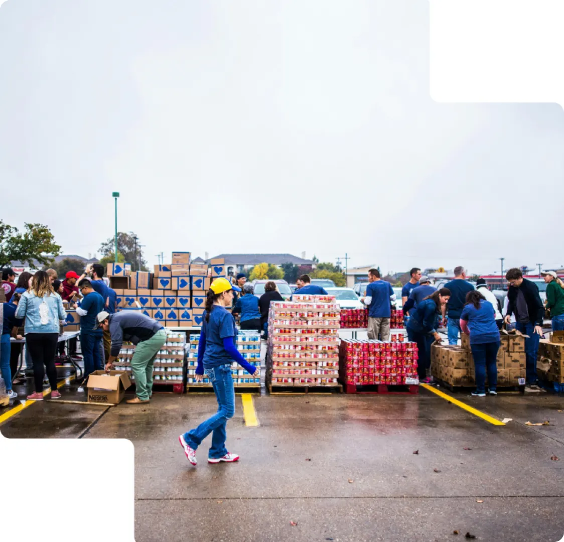 A photograph of volunteers packing cartons and tinned goods onto pallets in a wet car park.