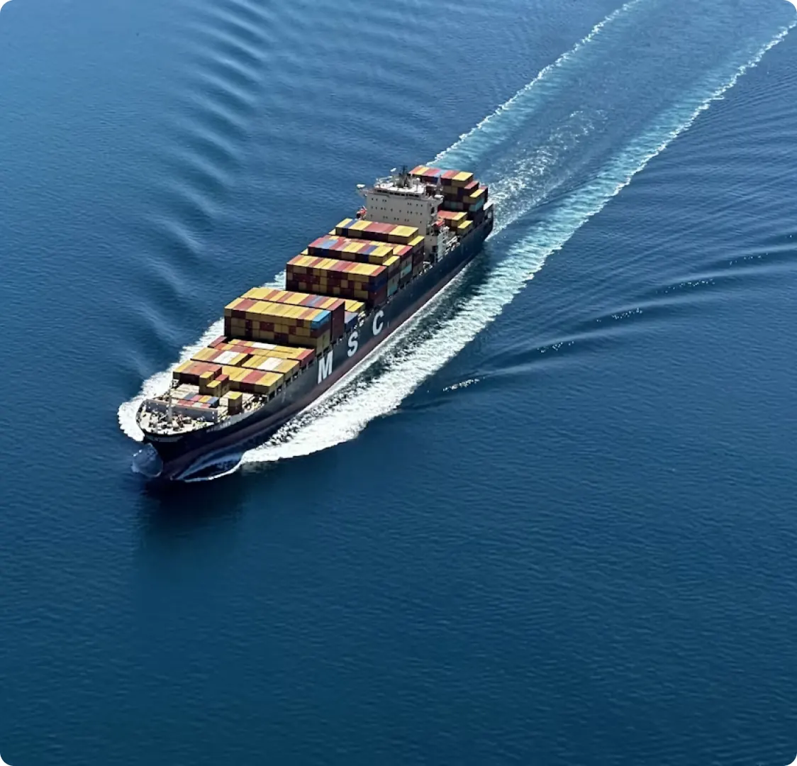 An aerial photograph of a loaded container ship under way on open water.