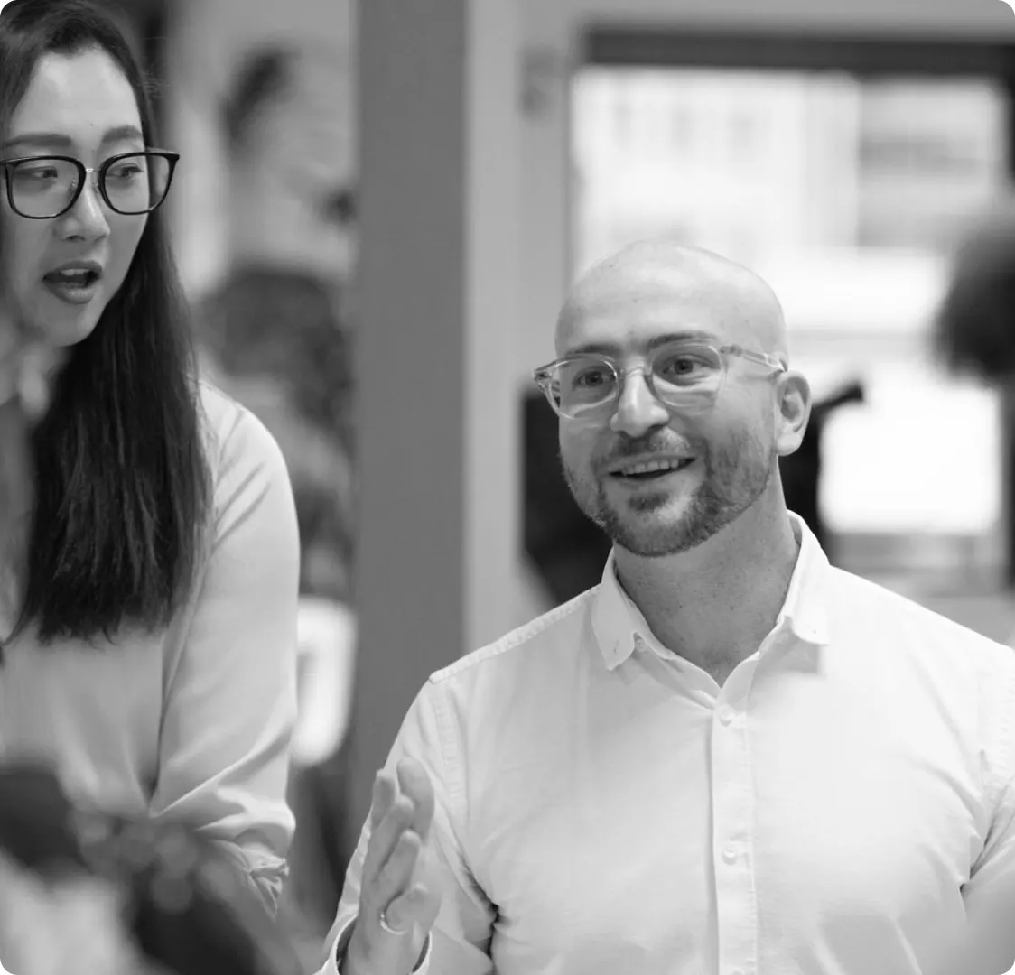 A black and white photograph of two colleagues talking in an open-plan office.