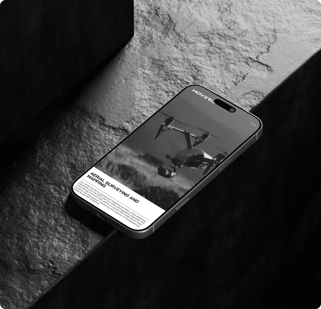 A phone lying on a stone ledge, showing the aerial surveying and mapping page with a drone photograph above the text.