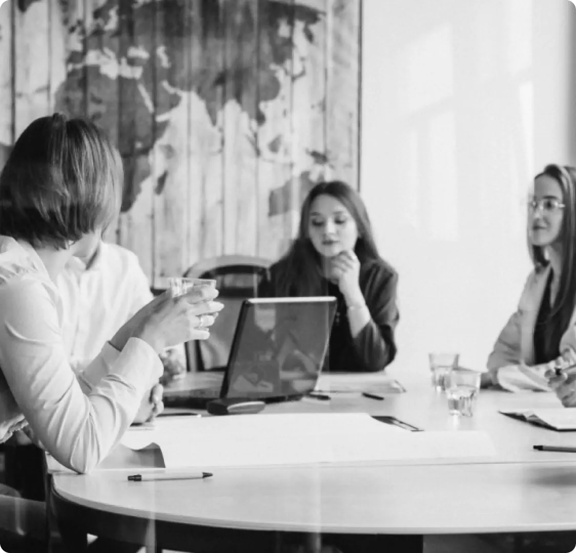 A black and white photo of four people around a boardroom table with a world map on the wall behind them.