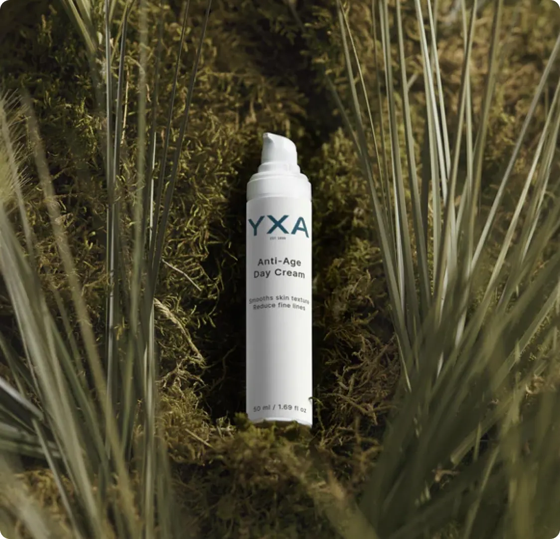 The Anti-Age Day Cream bottle lying in moss between tufts of dry grass.