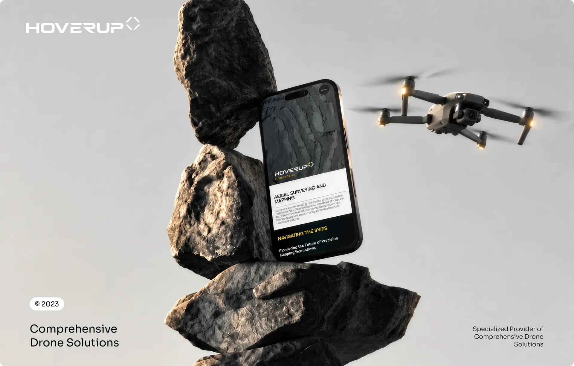A phone propped between stacked rocks showing the Hover Up aerial surveying and mapping page, with a drone flying beside it.
